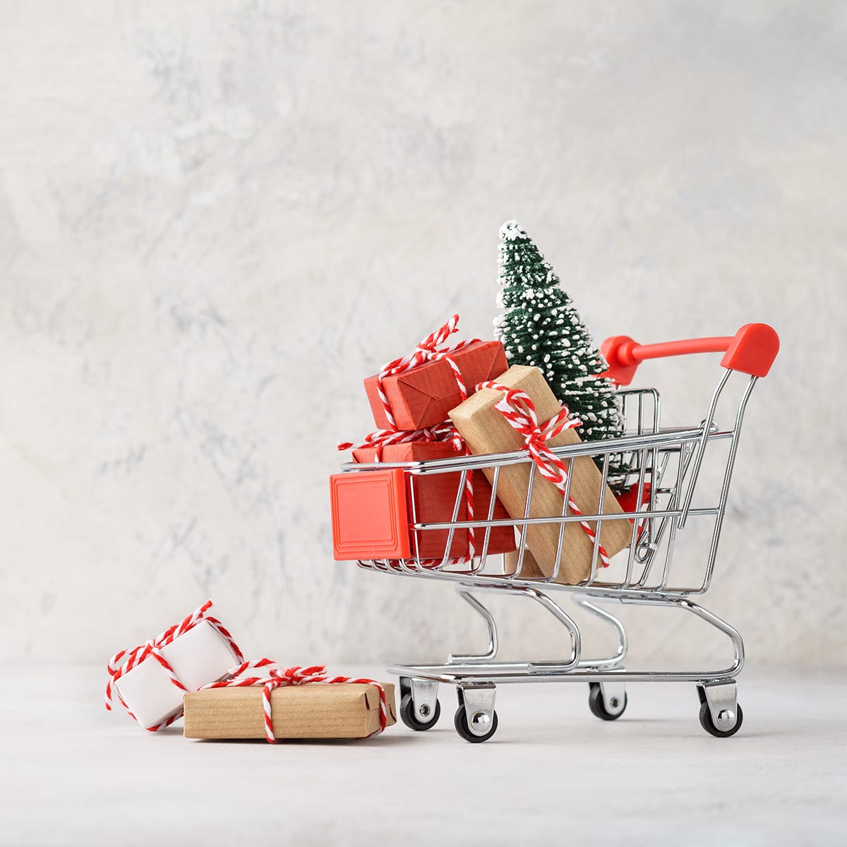 Shopping cart full of various gift boxes and a Christmas tree on light gray background. Christmas sale concept; blog: Gift Guide for Small Business Owners